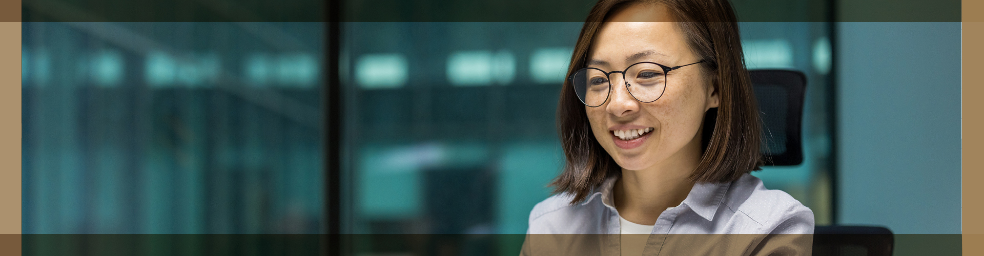Smiling woman with glasses working at a computer in a modern office setting.